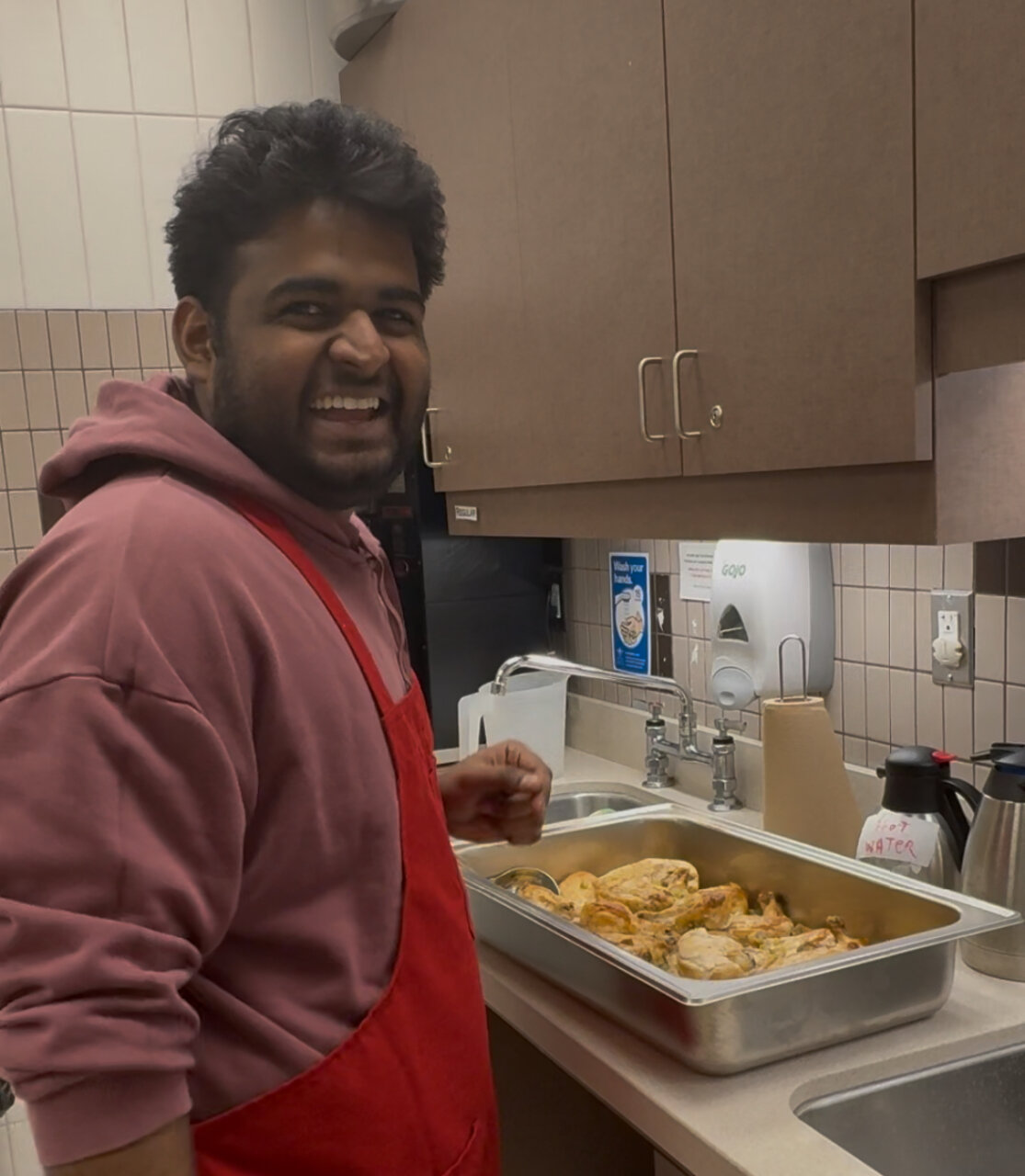 a black young adult in the kitchen smiling while preparing turkey that is in a pot on the counter in front of him